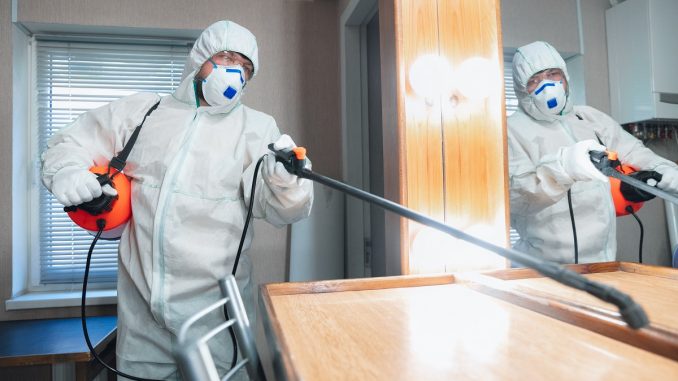Coronavirus Pandemic. A disinfector in a protective suit and mask sprays disinfectants in the house or office impresa pulizie
